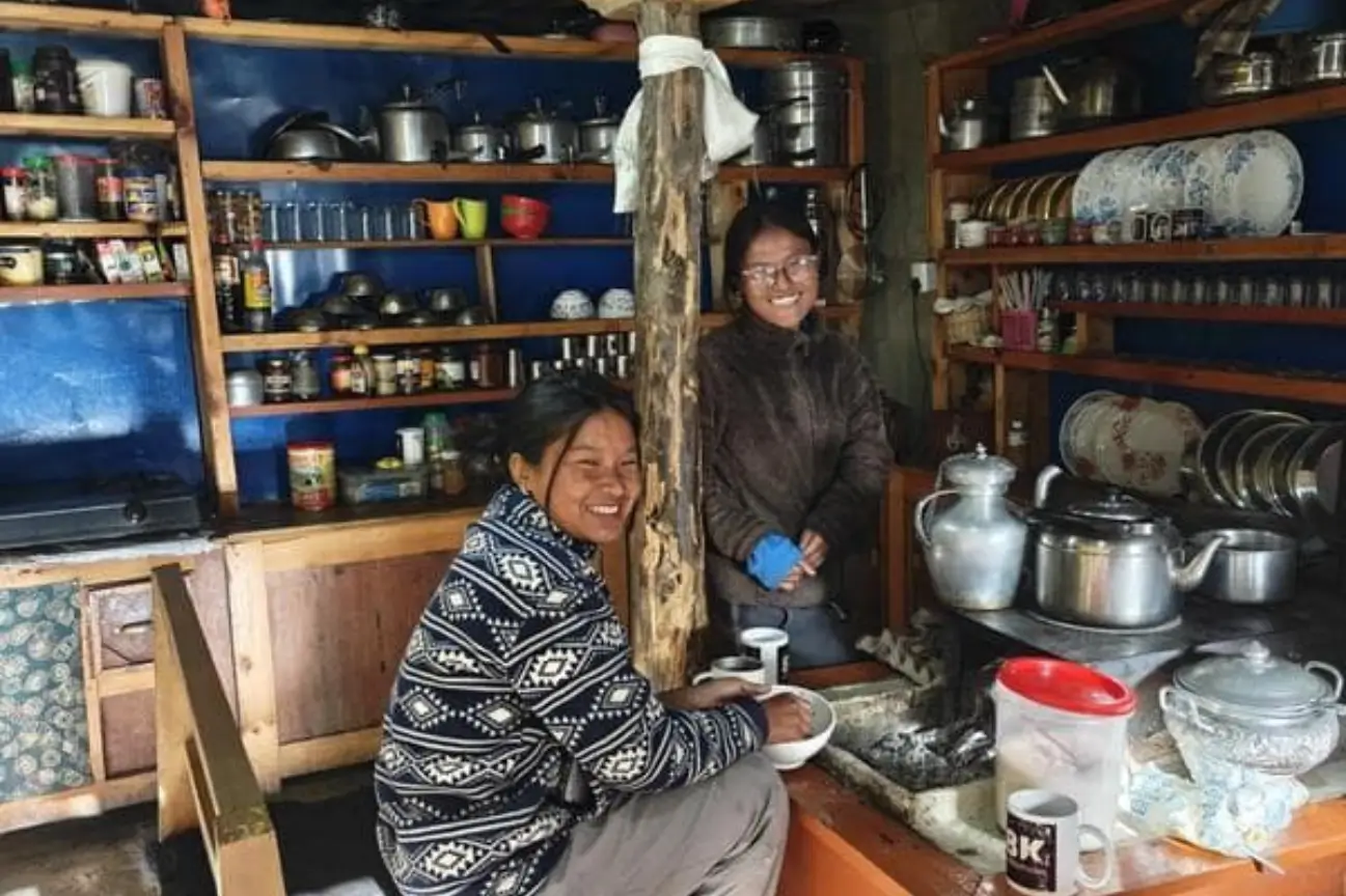 Two smiling local women inside a traditional kitchen stocked with utensils during the Annapurna Circuit Trek Tour.