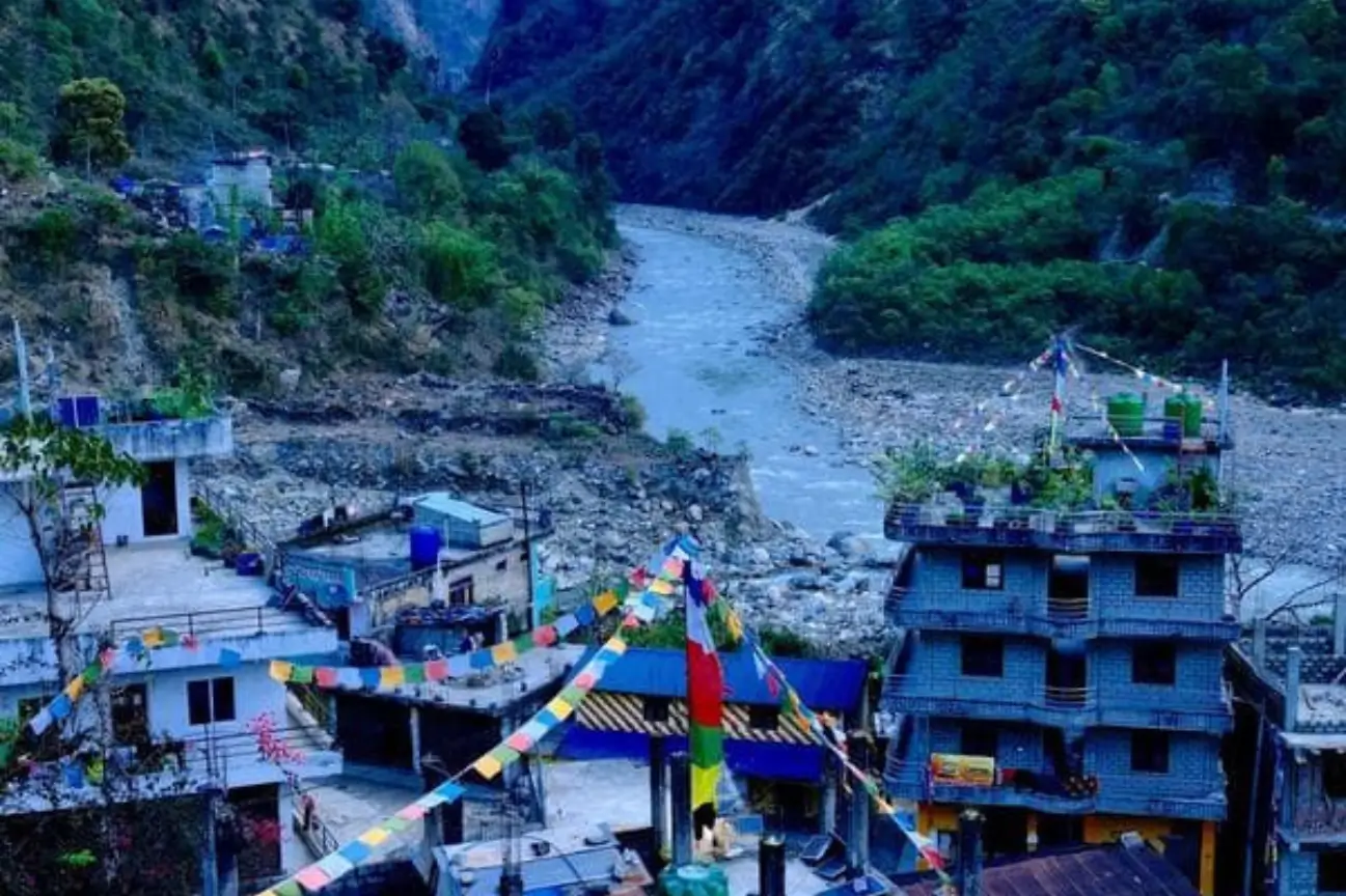 Colorful prayer flags strung across a mountain village settlement next to a flowing river during the Annapurna Circuit Trek Tour.