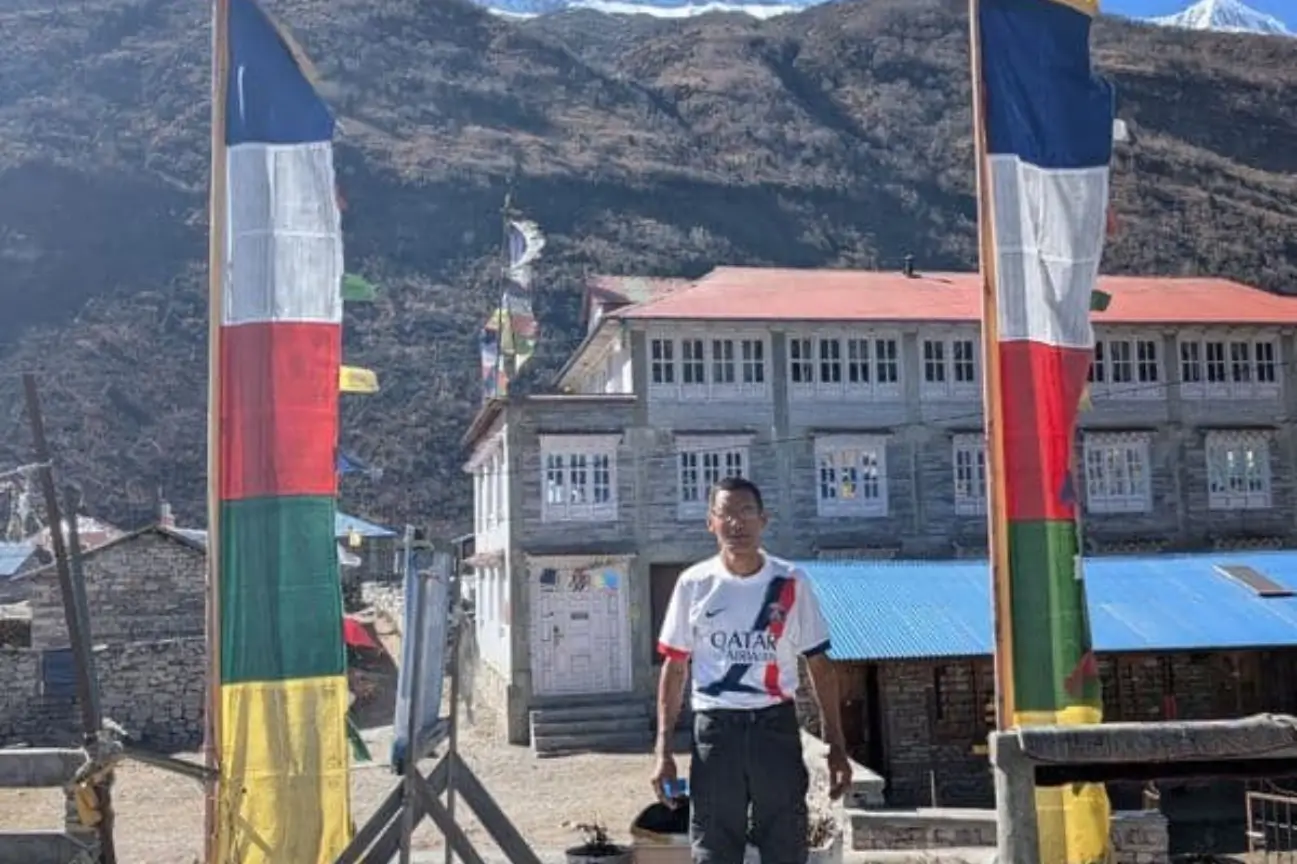 A local guide standing between tall ceremonial flags near a mountain lodge during the Annapurna Circuit Trek Tour.