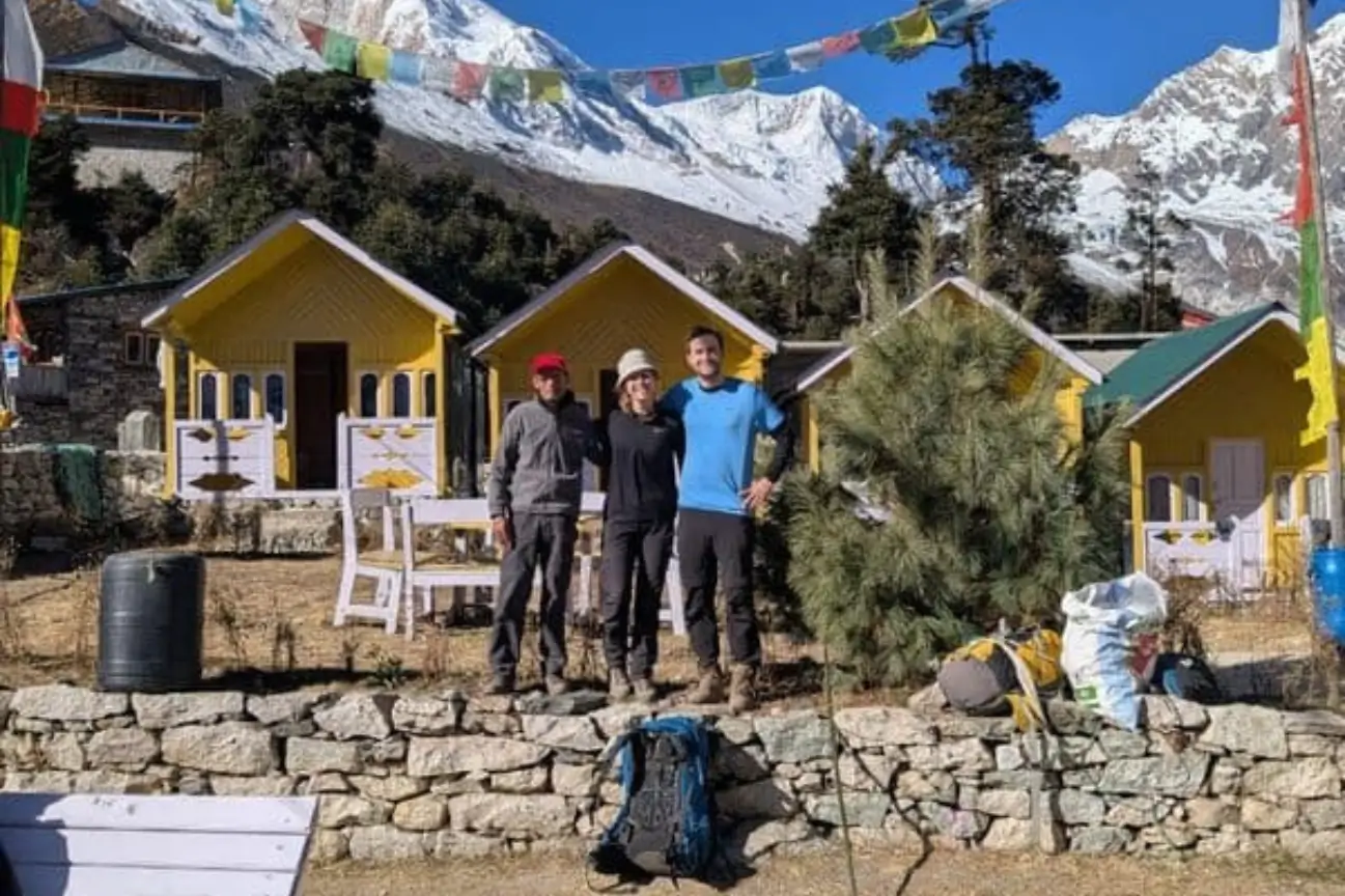 Trekkers posing in front of yellow mountain lodges with snow-capped Himalayan peaks and prayer flags during the Annapurna Circuit Trek Tour.